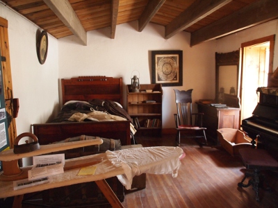 [One room dwelling with a bed in one corner, a rocking chair and a cradle by the window and an ironing board in the foreground.]